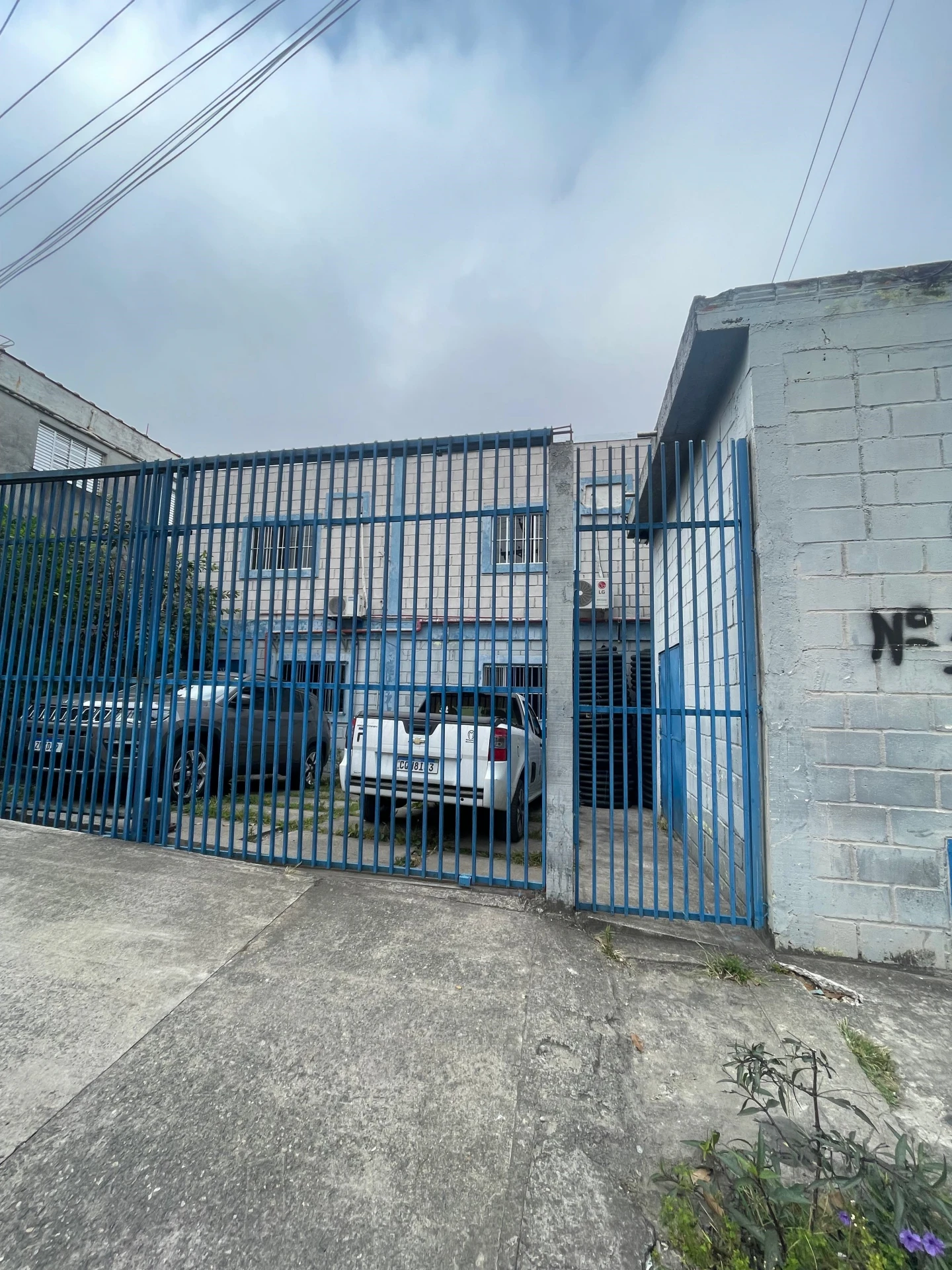 Foto de um portão azul de garagem, com alguns veículos estacionados nessa garagem